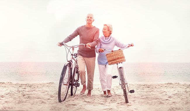 older man and woman walking bikes next to each other on the beach